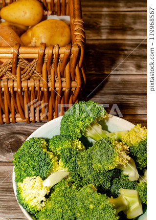 Broccoli pieces in bowl and potatoes in basket placed on table 119968567
