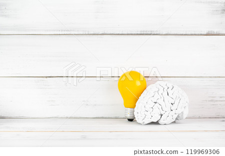 Innovative Mind: White Brain Model with Yellow Light Bulb on Rustic White Background 119969306