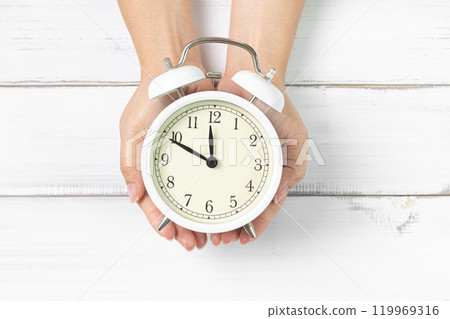 Time in Your Hands: Classic Clock Held Over White Wooden Background Time in Your Hands: Classic Clock Held Over White Wooden Background 119969316