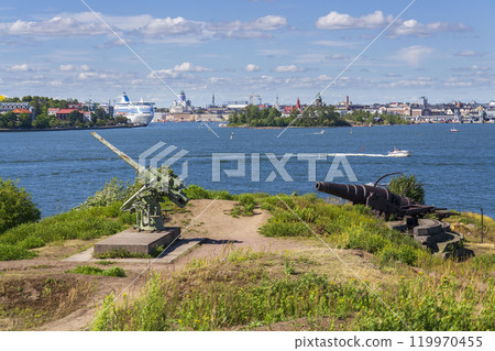 Cannons on island Lansi Mustasaari, Suomenlinna sea fortress with Helsinki city center in background, sunny summer day 119970455