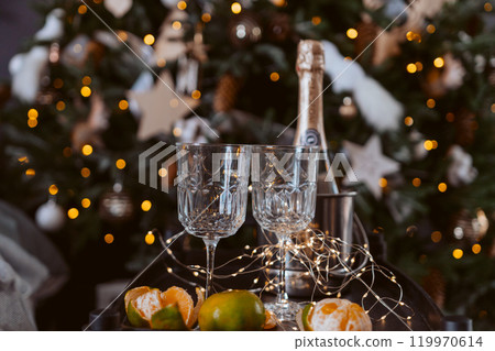 Champagne glasses, New Year decor. New Year's festive setting, family holidays.Two glasses of champagne are on the table against the background of New Year's decorated tree. 119970614