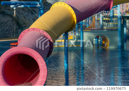 Waterpark Slide Pool Fun - Close-up of a pink and yellow water slide at a waterpark. The slide is situated above a blue pool. 119970675