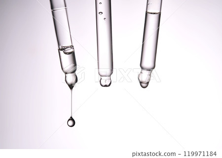 Three pipettes with a cosmetic product. Serum or fluid drips from one of them. 119971184