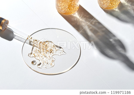 Golden glitter serum in glass petri dish with shadows on white background 119971186