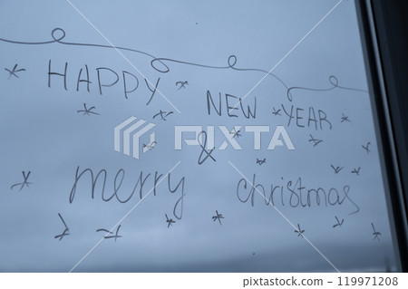 Sustainable responsible holiday decor. HAPPY NEW YEAR AND MERRY CHRISTMAS message painted on window glass indoor at home. Christmas winter decoration. White pattern. Snow art tracery on season. Diy Sustainable responsible holiday decor. HAPPY NEW YEAR AND MERRY CHRISTMAS message painted on window glass indoor at home. Christmas winter decoration. White pattern. Snow art tracery on season. Diy 119971208