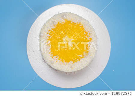 Delicious round yellow cake with orange slice and coconut flakes on blue background 119972575
