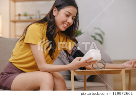 A woman is sitting on a couch and checking her blood pressure 119972661