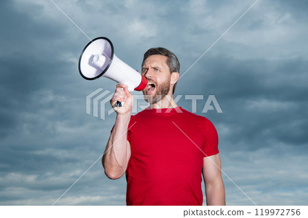 man in red shirt shout in loudspeaker on sky background 119972756
