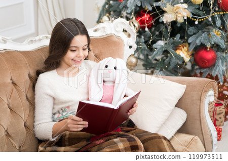 Literature club. Christmas spirit. Little reader enjoy reading at home. New year eve. Little girl reading Christmas story. Best Christmas book. Books shop commercial. Little smiling child read book 119973511