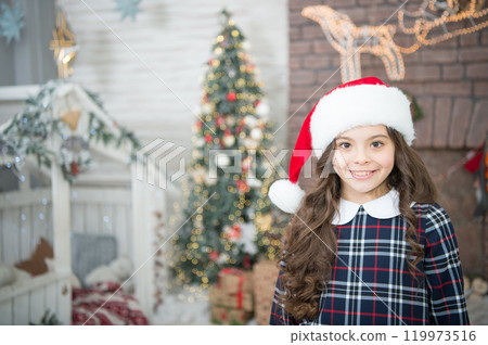 Small girl at home garland lights. Kid relaxing cozy garland. Christmas tree decorations interior background. Turn on garland for magic atmosphere. Illumination concept. Happy winter holidays 119973516