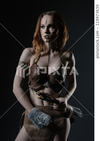 A figure dressed in tribal attire holds a bow and arrows in a dramatic pose 119973630