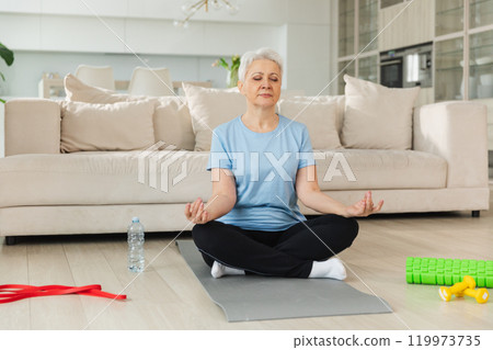 Yoga mindfulness meditation. Senior adult mature woman practicing yoga at home. Mid age old lady sitting in lotus pose on yoga mat meditating relaxing. Older middle aged woman doing breathing practice 119973735