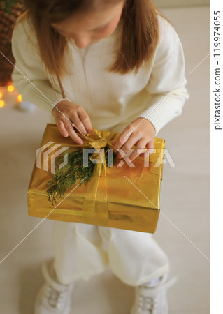 a child eagerly unwrapping a present beneath a beautifully decorated Christmas tree. The look of excitement and curiosity on the child's face adds to the magic of the moment.  119974055