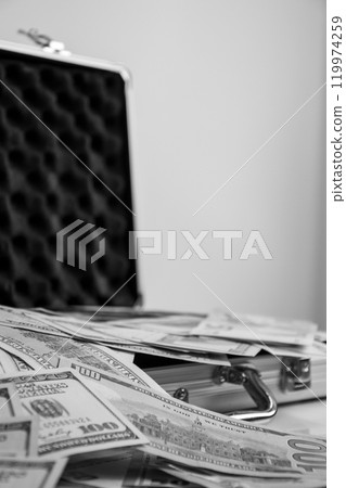 A black and white image of an open metal briefcase with stacks of cash spilling out 119974259
