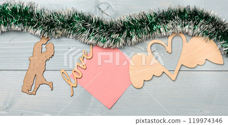 Tinsel with christmas ornaments and blank paper note wooden background. Merry christmas concept. Christmas ornaments and wooden silhouette couple and heart toy green tinsel. Christmas ornaments Tinsel with christmas ornaments and blank paper note wooden background. Merry christmas concept. Christmas ornaments and wooden silhouette couple and heart toy green tinsel. Christmas ornaments 119974346