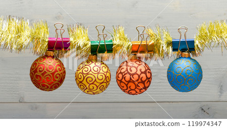 Christmas ornaments concept. Balls with ornaments hang on shimmering tinsel. Pick colorful decor for christmas tree. Tinsel with pinned christmas ornaments on wooden background Christmas ornaments concept. Balls with ornaments hang on shimmering tinsel. Pick colorful decor for christmas tree. Tinsel with pinned christmas ornaments on wooden background 119974347