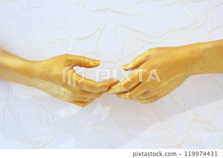 Two golden-colored hands gently clasp each other, symbolizing connection and unity. The hands interact in a graceful manner against a light background, creating a serene and elegant atmosphere. 119974431