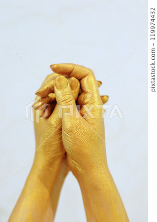 Two golden-colored hands gently clasp each other, symbolizing connection and unity. The hands interact in a graceful manner against a light background, creating a serene and elegant atmosphere. Two golden-colored hands gently clasp each other, symbolizing connection and unity. The hands interact in a graceful manner against a light background, creating a serene and elegant atmosphere. 119974432