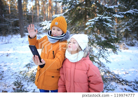 A brother and sister are joyfully engaged in a video call, set against the stunning backdrop of a snowy forest. The scene captures their laughter and connection despite the distance, with snow-covered 119974777