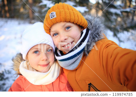 A lively scene of children happily taking a selfie in front of a picturesque snowy forest. Their bright smiles and playful poses reflect the joy of winter adventures and the fun of capturing memories A lively scene of children happily taking a selfie in front of a picturesque snowy forest. Their bright smiles and playful poses reflect the joy of winter adventures and the fun of capturing memories 119974785