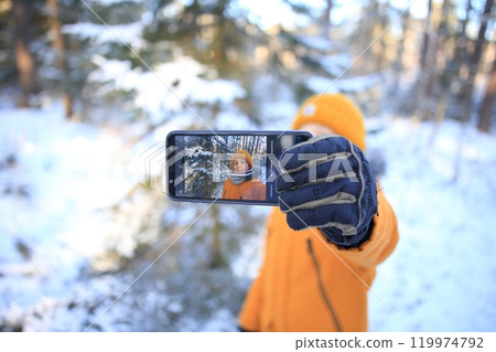 A young man takes a selfie against the breathtaking backdrop of a snow-covered forest.  119974792