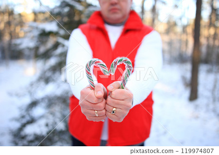a pair of hands holding colorful heart-shaped lollipops, set against a stunning winter landscape in a forest. a pair of hands holding colorful heart-shaped lollipops, set against a stunning winter landscape in a forest. 119974807