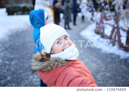 a close-up portrait of a delighted child bundled up in cozy winter clothing. With a bright smile and rosy cheeks, the child radiates joy and warmth against a backdrop of winter scenery 119974809