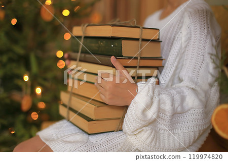 books held in hands, set against the backdrop of a beautifully decorated Christmas tree books held in hands, set against the backdrop of a beautifully decorated Christmas tree 119974820