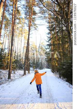 A young man walks leisurely through a picturesque snowy forest, surrounded by towering trees blanketed in fresh snow. A young man walks leisurely through a picturesque snowy forest, surrounded by towering trees blanketed in fresh snow. 119976027