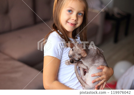 A joyful scene of a young girl playing with her adorable Sphynx cats. The unique, hairless cats are playfully interacting with her, creating a delightful atmosphere filled with laughter and affection. A joyful scene of a young girl playing with her adorable Sphynx cats. The unique, hairless cats are playfully interacting with her, creating a delightful atmosphere filled with laughter and affection. 119976042