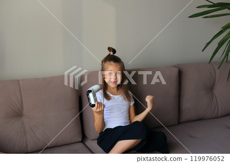 A young girl is intensely focused and emotionally engaged as she plays a video game on the television. Her expressions of joy, concentration, and excitement convey the immersive experience of gaming. A young girl is intensely focused and emotionally engaged as she plays a video game on the television. Her expressions of joy, concentration, and excitement convey the immersive experience of gaming. 119976052
