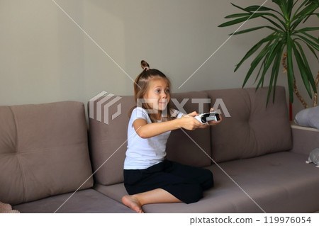 A young girl is intensely focused and emotionally engaged as she plays a video game on the television. Her expressions of joy, concentration, and excitement convey the immersive experience of gaming.  119976054