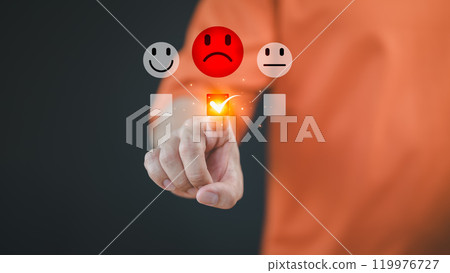 Engaging in an online customer feedback survey, a male user touching to display an angry emoticon on a virtual screen, sharing their opinion and reviewing service satisfaction. 119976727