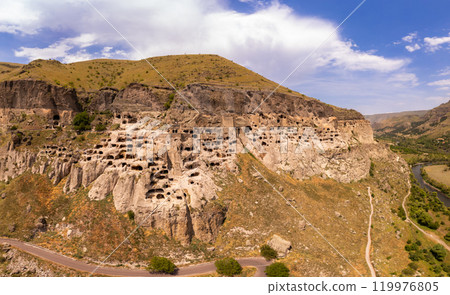 Aerial top view of Vardzia city on sunny summer day. Ancient cave monastery in Erusheti Mountain rocks at Kura River. Monument of medieval Georgian architecture, carved in rough rock. Georgia, Europe. 119976805