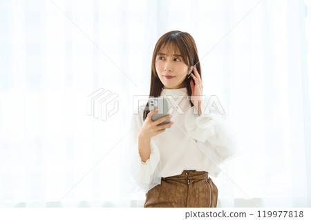 A young woman wearing earphones and looking at her smartphone 119977818