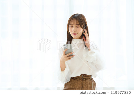 A young woman wearing earphones and looking at her smartphone 119977820
