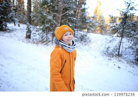 A young man walks leisurely through a picturesque snowy forest, surrounded by towering trees blanketed in fresh snow.  119978236