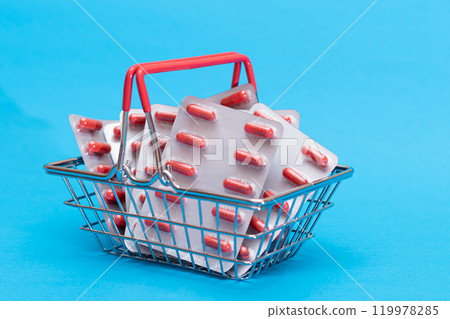 Pills and Capsules in Shopping Basket on Blue Background Pills and Capsules in Shopping Basket on Blue Background 119978285