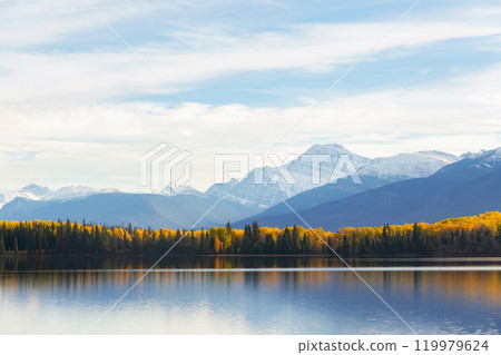 Tranquil lake waters at the mountain foot in autumn forest. Tranquil lake waters at the mountain foot in autumn forest. 119979624