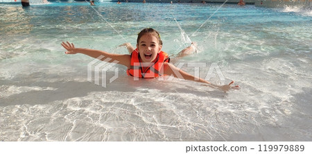 Joyful child swimming in a pool with a bright orange life vest 119979889