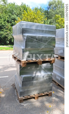 Pallets of shrink-wrapped goods outdoors on a sunny day near trees 119979905