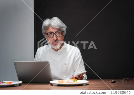 A chef improves a dish by looking at a computer 119980645