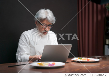 A chef improves a dish by looking at a computer 119980647