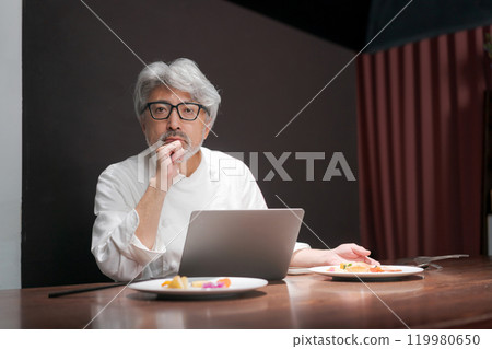 A chef improves a dish by looking at a computer 119980650