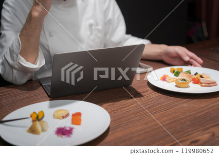 A chef improves a dish by looking at a computer 119980652