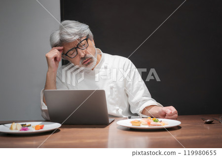 A chef improves a dish by looking at a computer 119980655
