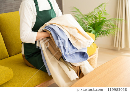 穿著圍裙的中高級女性在客廳的沙發上疊衣服 119983038