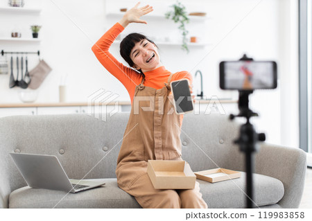 Young woman unboxing new smartphone during live streaming session Young woman unboxing new smartphone during live streaming session 119983858
