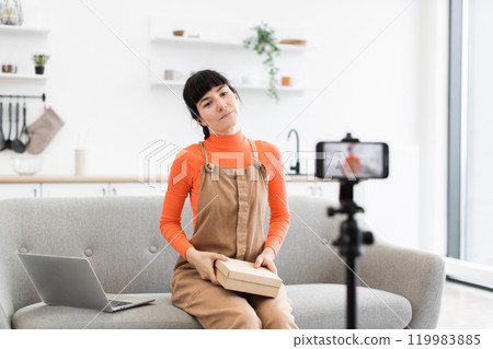 Young woman recording unboxing video in modern home studio Young woman recording unboxing video in modern home studio 119983885