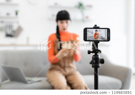 Caucasian female blogger unwrapping gift during online video recording session 119983891